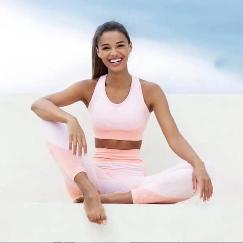 Femme en tenue d’entraînement rose, assise et souriante.