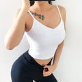 Femme portant un haut blanc et un pantalon foncé, avec un tatouage visible sur l’épaule.