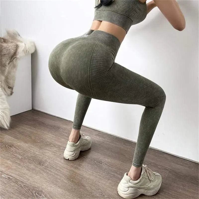 Femme portant un legging d’entraînement vert olive et un haut de forme assorti, posant avec une jambe pliée.