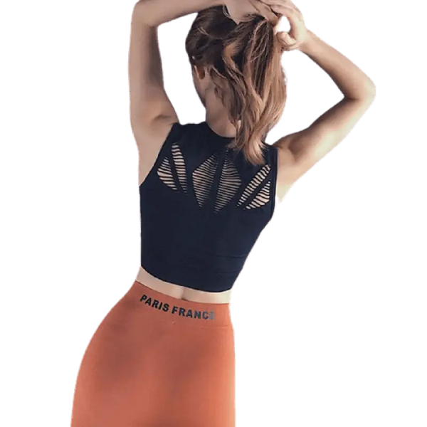 Femme portant un crop top noir et un legging orange, les mains dans les cheveux.