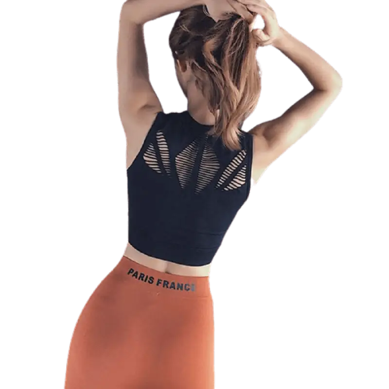 Femme portant un crop top noir et un legging orange, les mains dans les cheveux.